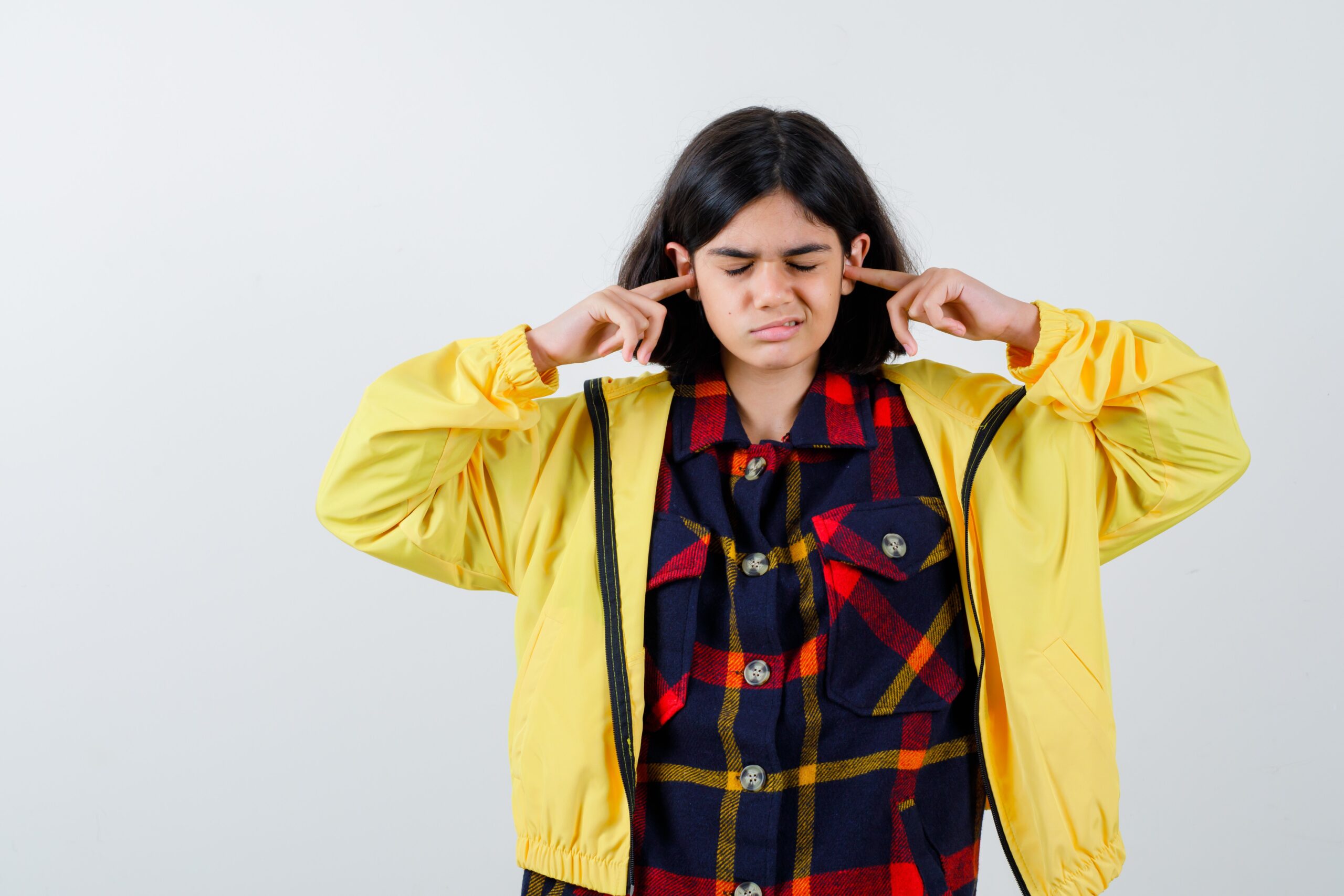 Little Girl Checked Shirt Jacket Plugging Ears With Fingers Looking Annoyed Front View 1 Scaled